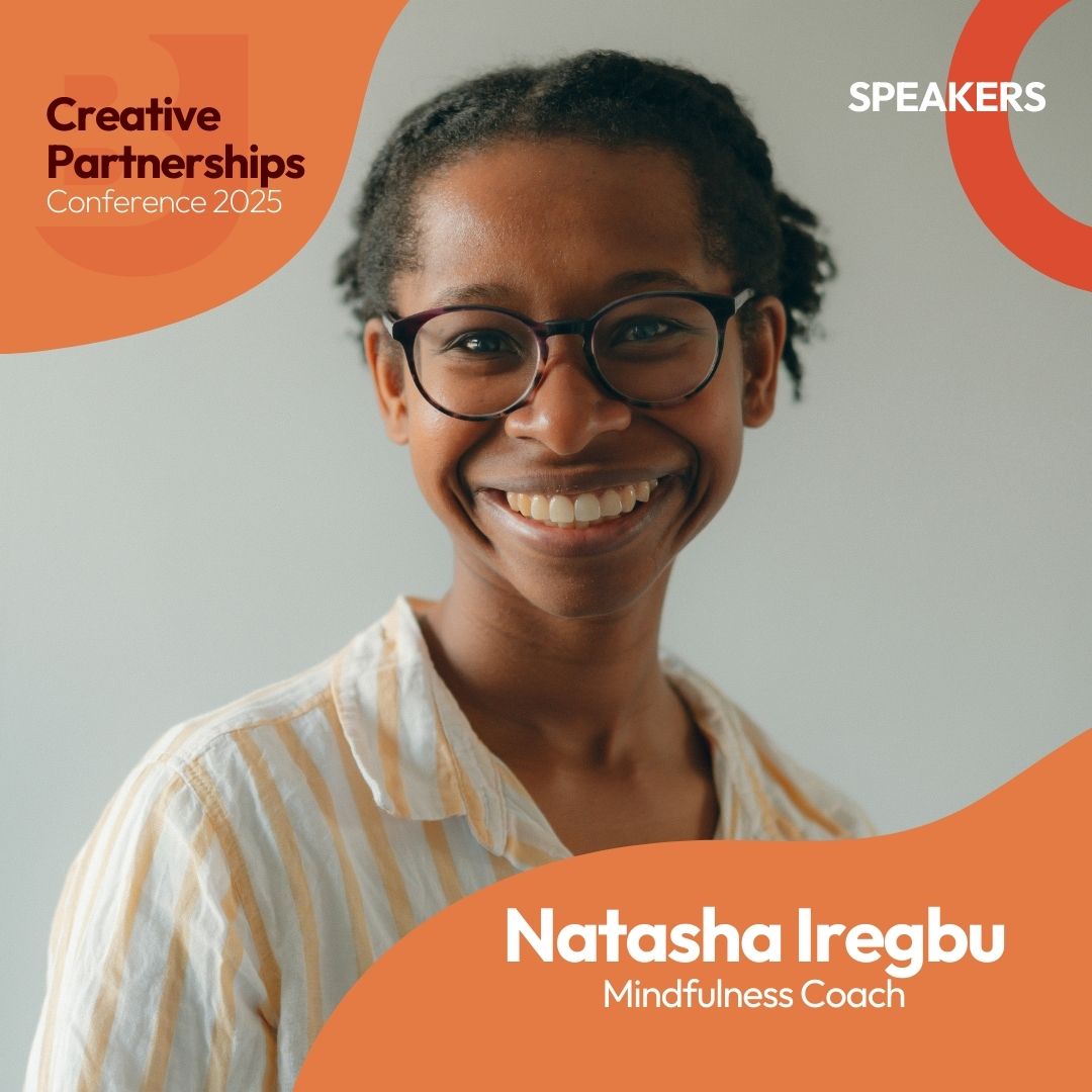 A young black woman with black glasses and a big smile is looking at a camera. She is wearing a white cotton shirt with light orange stripes.  In a neutral, grey background. Text reads: Creative Partnerships Conference 2025. Speakers. Natasha Iregbu. Mindfulness Coach.