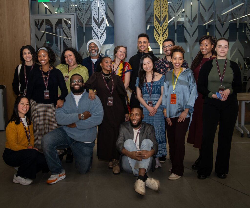 15 members of Be United Team and Board are standing in front of a glass conference room, smiling.